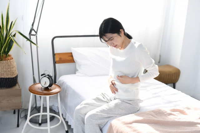 ベッド上でお腹を押さえる女性