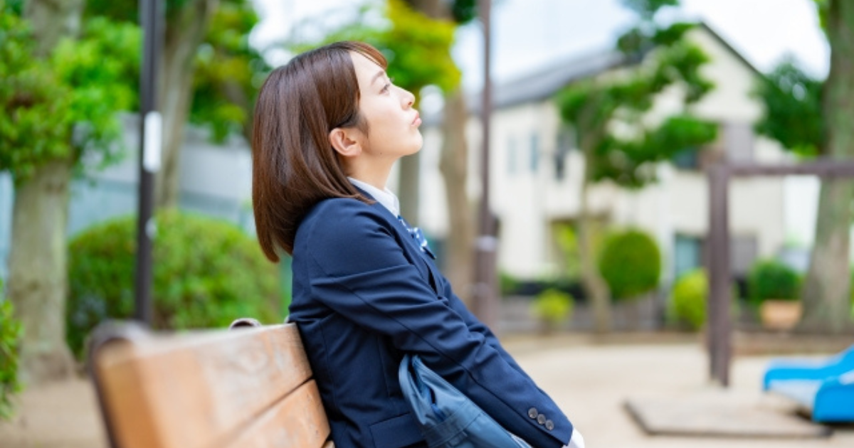 公園のベンチで空を見上げる女子高生