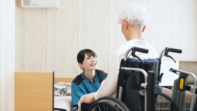 車椅子に乗った高齢女性に微笑みかける介護士